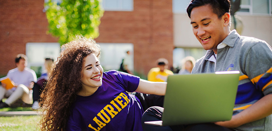 Two students outside looking at a laptop