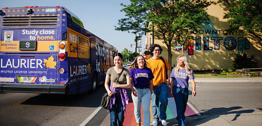 group of students next to a Laurier branded bus walking downtown Milton