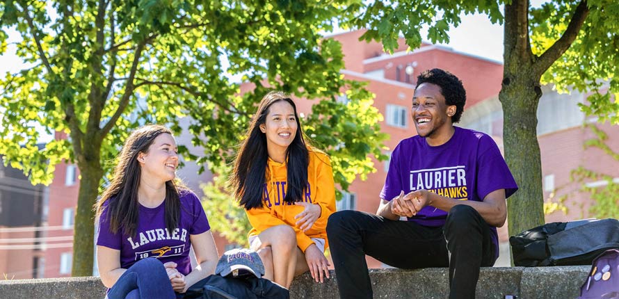 students smiling and sitting outside on campus in the summer