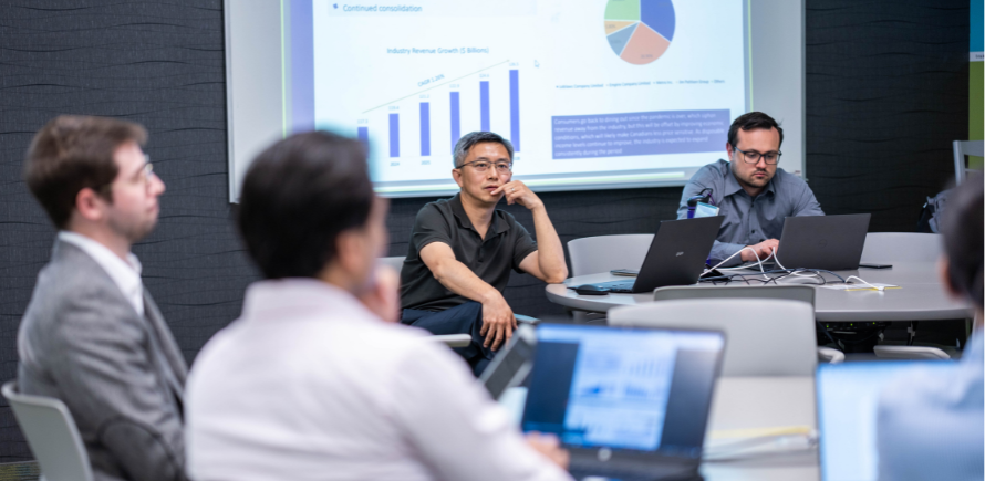 Students sat around tables with laptops with charts on projector screens in the background